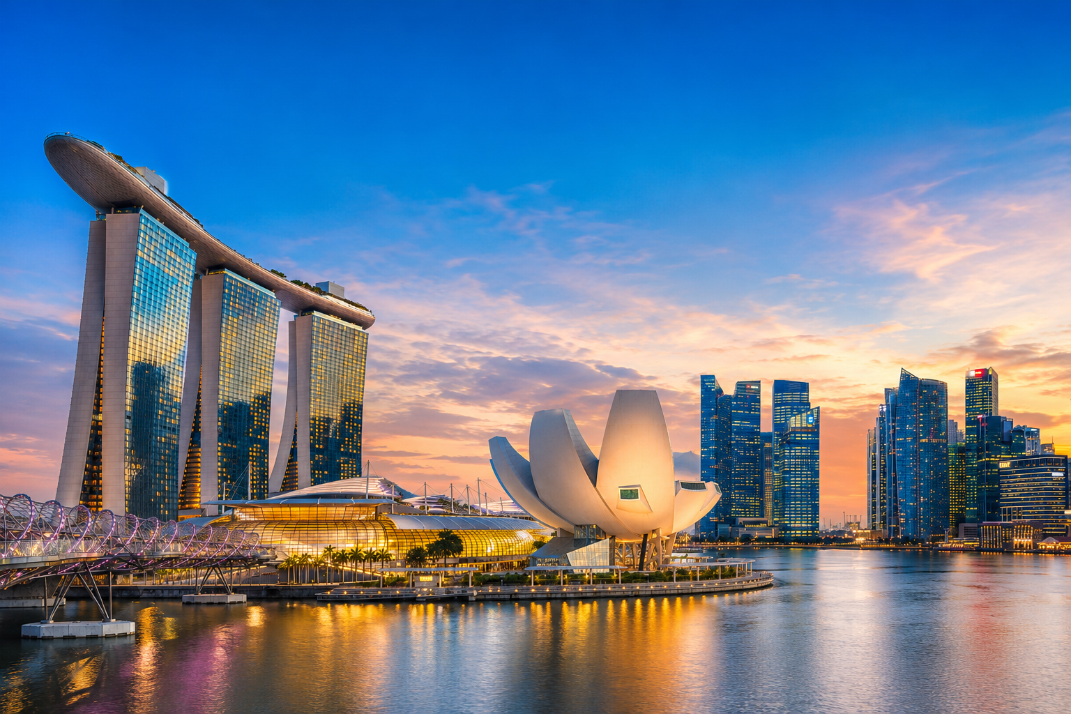 Panoramic view of Singapore's Marina Bay skyline at sunset, featuring Marina Bay Sands, the ArtScience Museum, Helix Bridge, and the city's modern waterfront skyline reflected in calm waters.